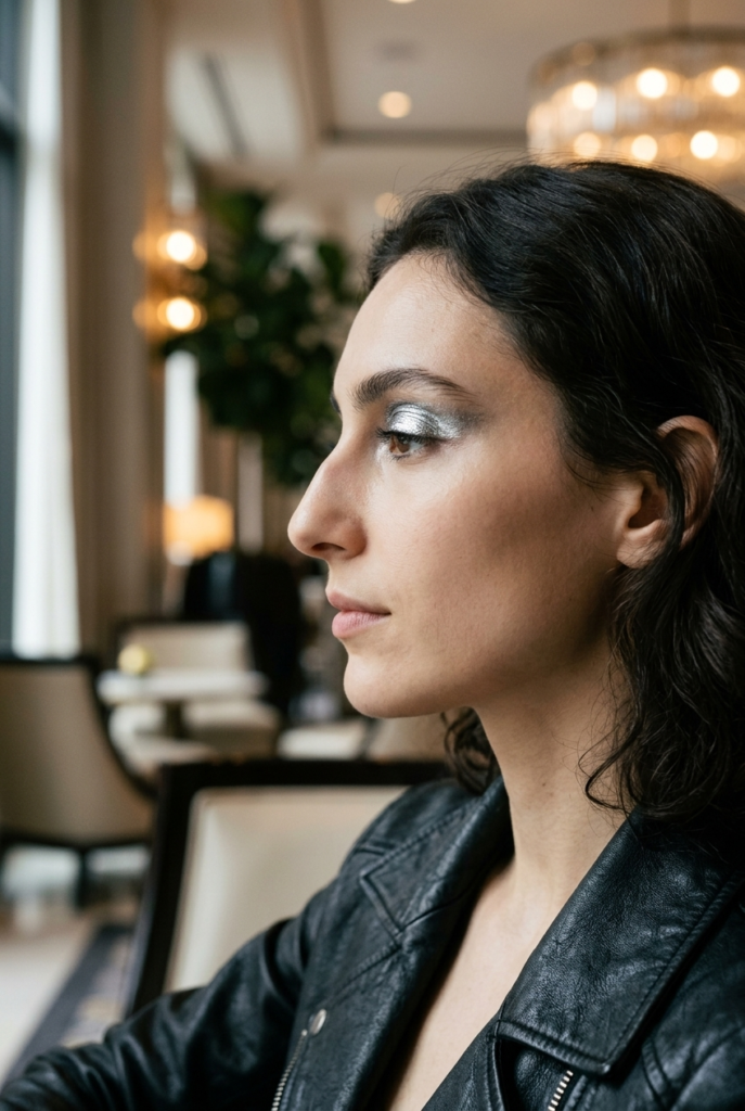Woman with chrome metallic silver eyelids in side profile in a hotel lobby wearing a leather jacket