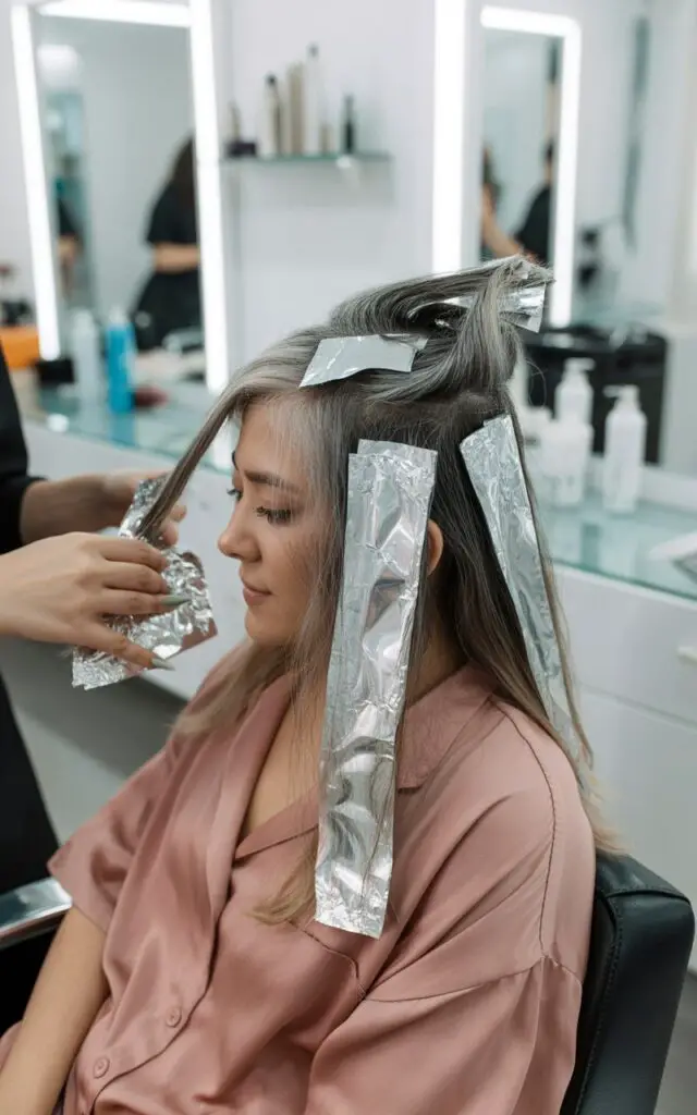 Hair colorist applying full foil highlights to woman with gray hair transition