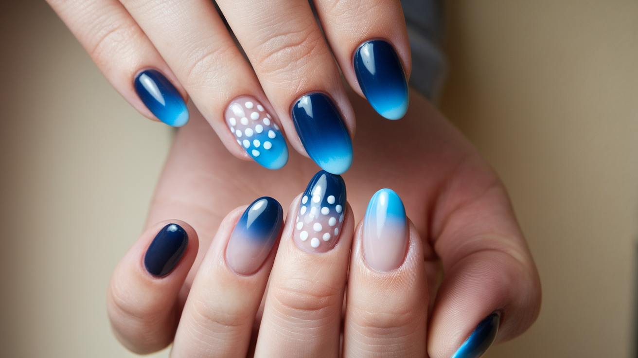 A photo of a woman's hand with ombre nails. The nails transition from a dark blue at the tips to a light blue at the base. There are also small, white polka dots on each nail. The nails are well-groomed, with a smooth and shiny finish. The background is a beige wall.