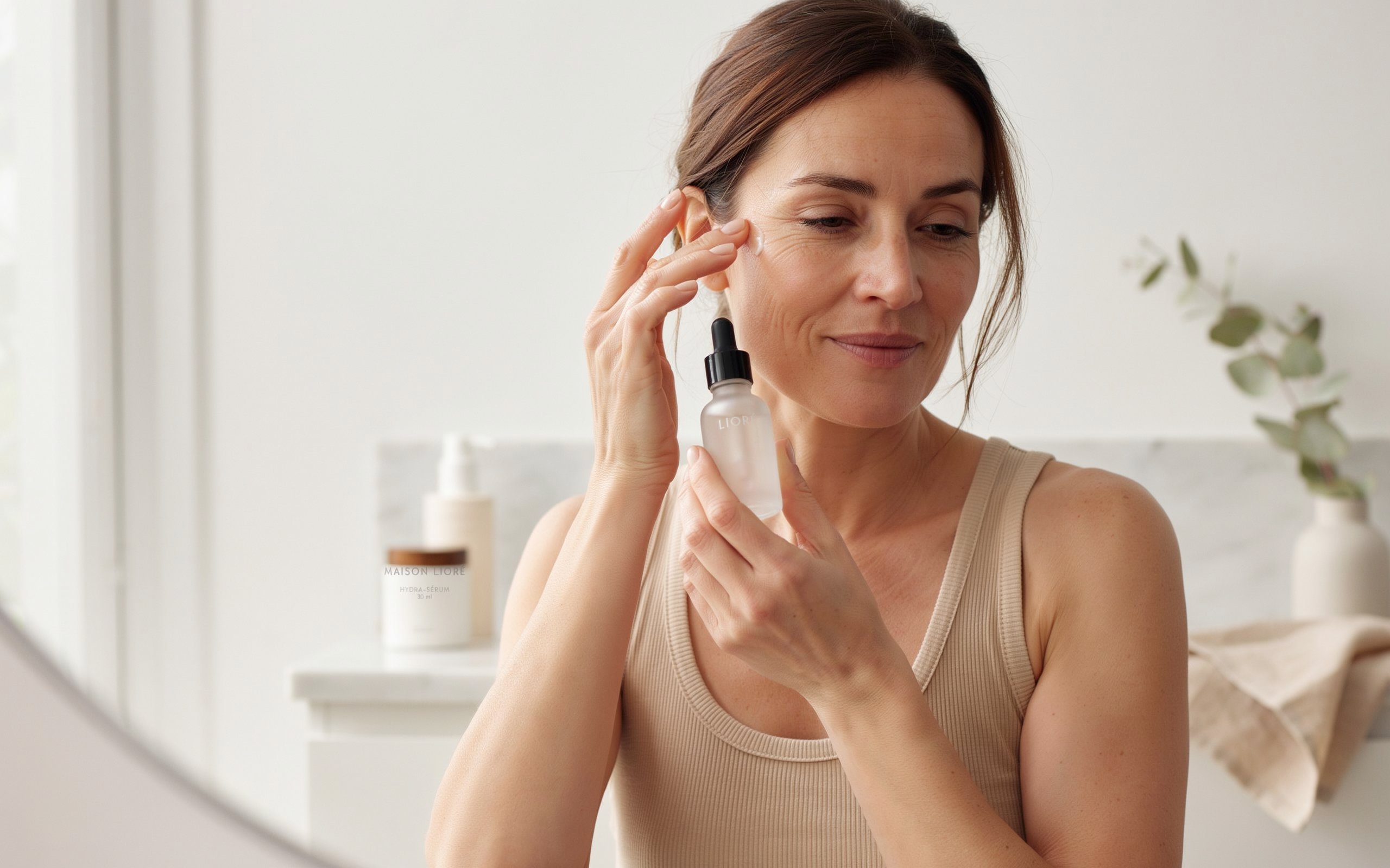 attractive woman in her early 40s with naturally glowing, healthy skin applying a serum to her face with her fingertips